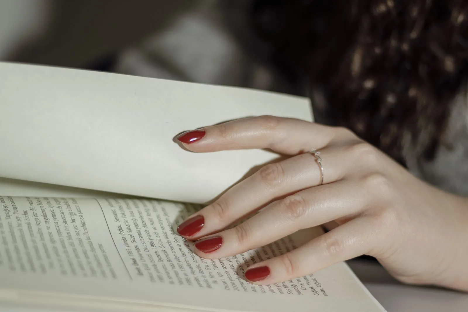 A woman's hand with red nails and a ring flipping pages of an open book.